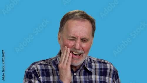 Aged amture senior caucasian man suffering from toothache. Touching cheek because of pain. Isolated on blue. photo