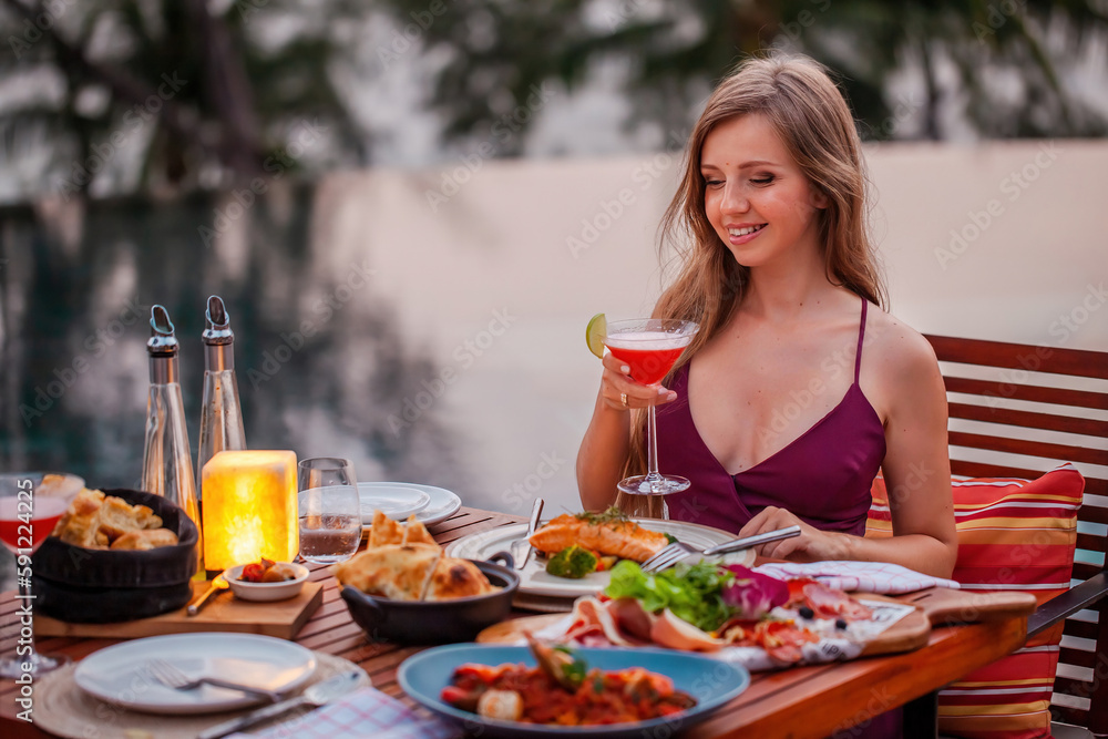 Elegant attractive smiling woman on romantic dinner in luxury gourmet restaurant. Happy young lady with a glass of cocktail in fine dining outdoor restaurant. Sexy elegant girl celebrating holiday. Elegant attractive smiling woman on romantic dinner in luxury gourmet restaurant. Happy young lady with a glass of cocktail in fine dining outdoor restaurant. Sexy elegant girl celebrating holiday.