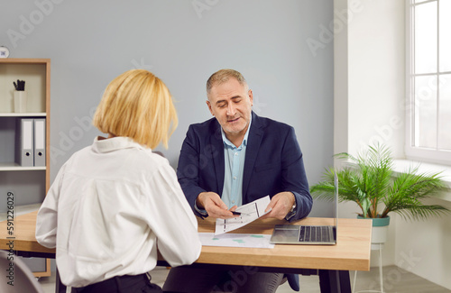 Real estate agent and customer meeting for house investment. Woman client and male lawyer sitting at desk in office discussing home architectural plan. Real estate, property value estimation