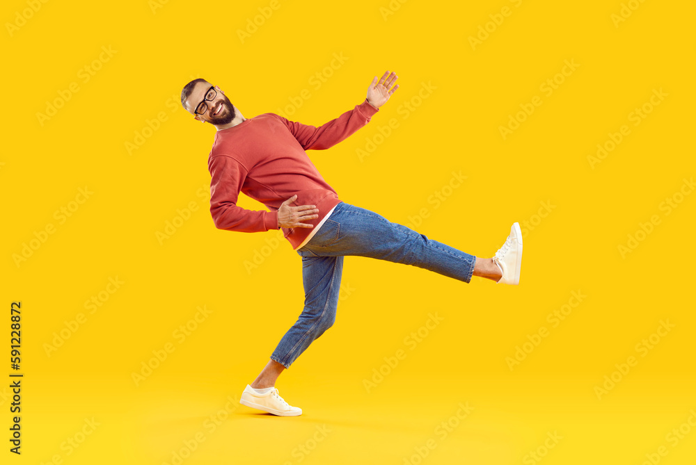 Cheerful, funny and humorous young man takes big wide step on orange background. Handsome stylish man in casual sweatshirt, jeans and sneakers is taking step while looking at camera. Full length.
