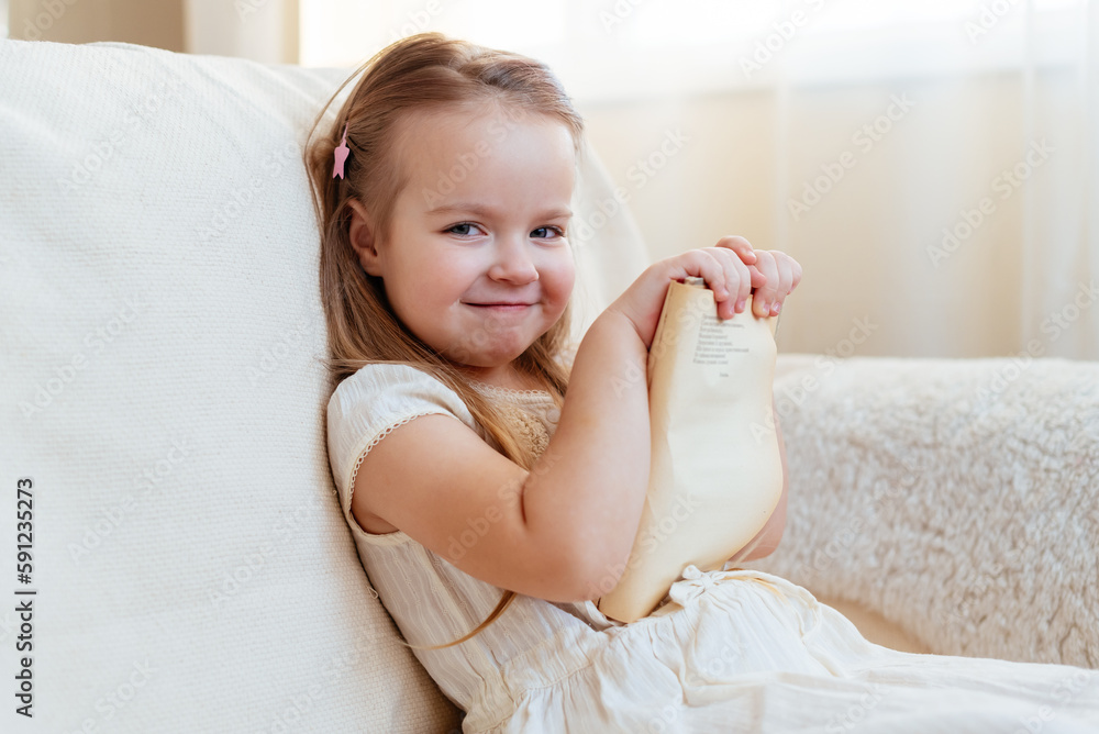 Little cute blond girl reading book siting on a sofa. Child reading, dreaming and imagination development. International Children's Book Day. Kids Love to reading. World Book Day Little cute blond girl reading book siting on a sofa. Child reading, dreaming and imagination development. International Children's Book Day. Kids Love to reading. World Book Day