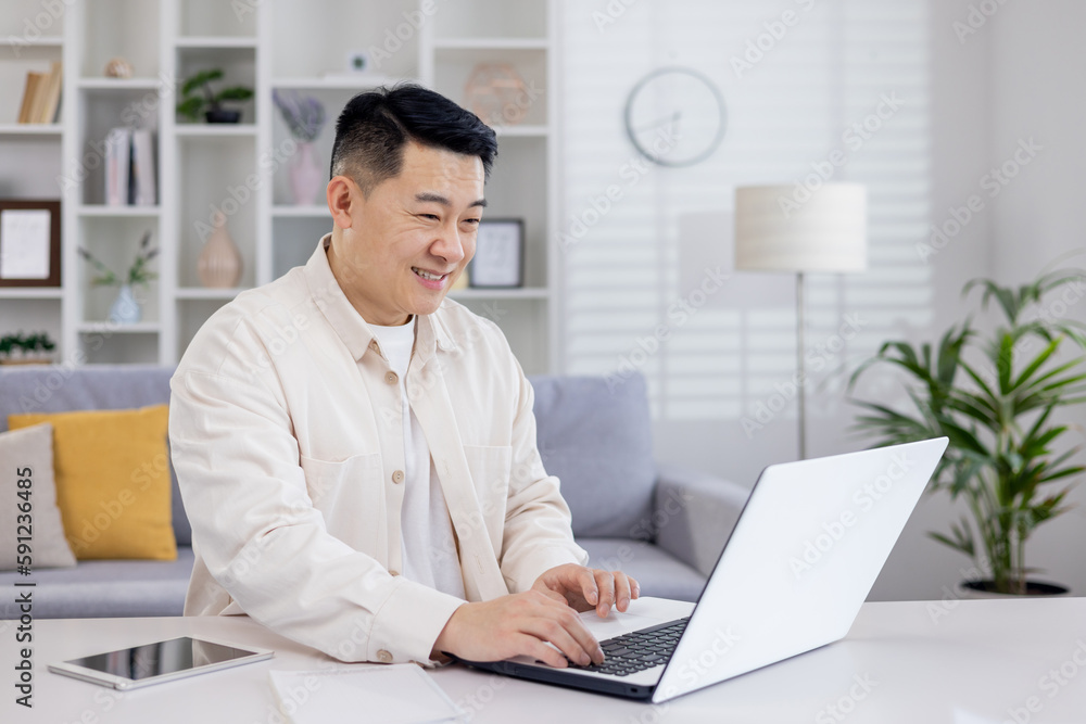 Smiling Asian man, businessman, freelancer, student working studying at home using laptop, Sitting at table and talking on video call, typing.