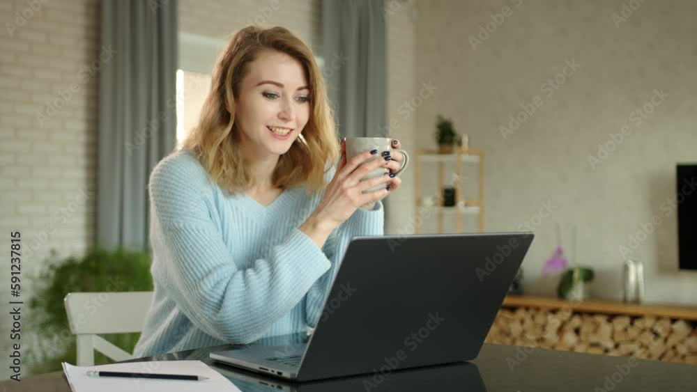 Pretty young blonde is having conversation via video link on laptop at home in a well-furnished room. Timelapse. The woman holds cup of tea in hands. High quality 4k footage Pretty young blonde is having conversation via video link on laptop at home in a well-furnished room. Timelapse. The woman holds cup of tea in hands. High quality 4k footage