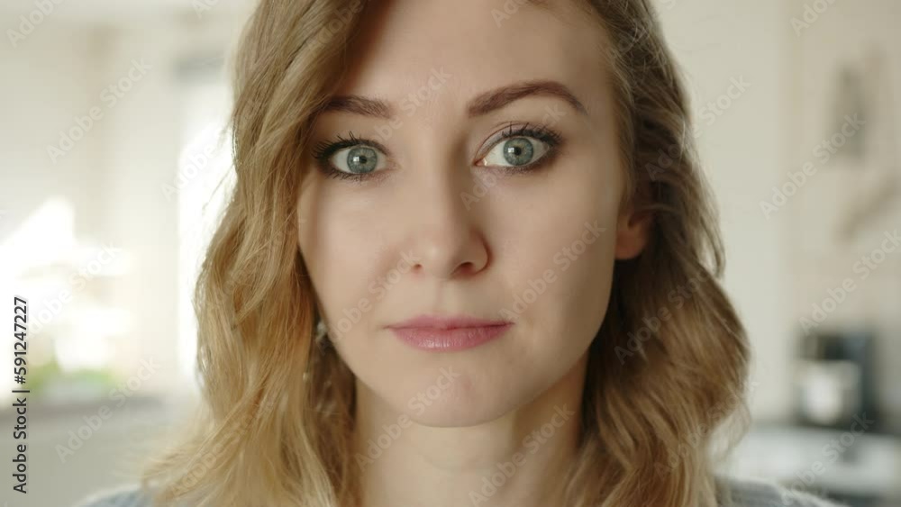 Close up of beautiful serious blonde with expressive eyes, blurry background of interior. The woman has minimum of make-up, pale pink lipstick. High quality 4k footage Close up of beautiful serious blonde with expressive eyes, blurry background of interior. The woman has minimum of make-up, pale pink lipstick. High quality 4k footage