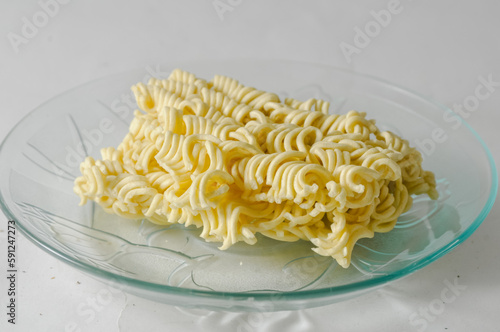 Uncooked instant noodles cut in half on a small plate isolated on a white background