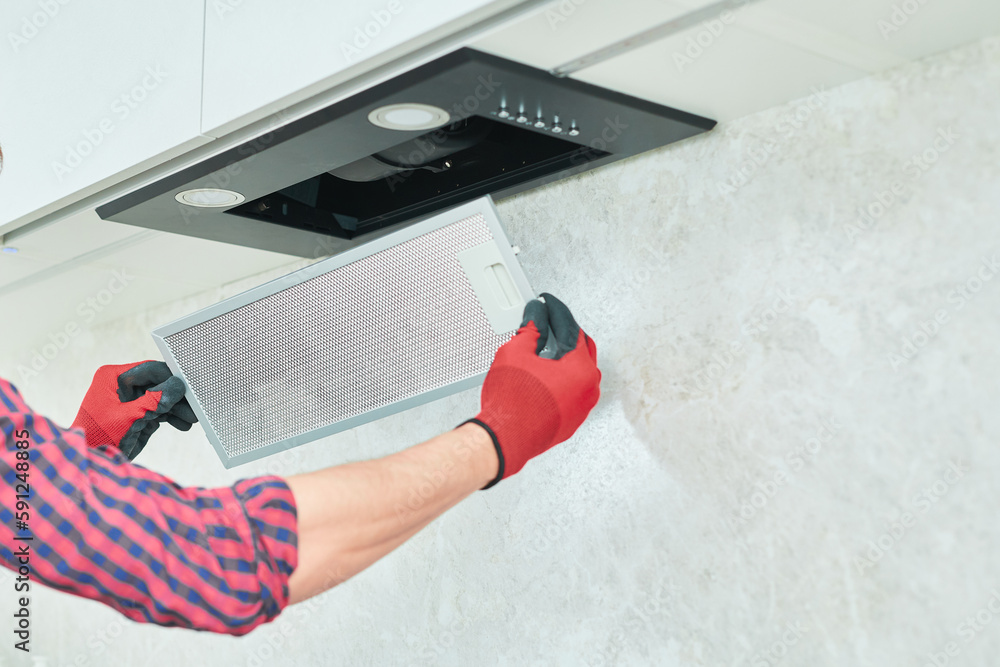 Mans hands removing a filter from cooker hood for cleaning or service