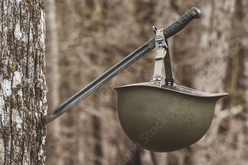 Fotografi Vintage M1 army helmet hanging on bayonet