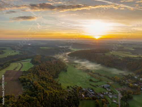 Aerial drone Sunrise view Above autumn colored forest and Valleys in Luxembourg, covered in morning fog