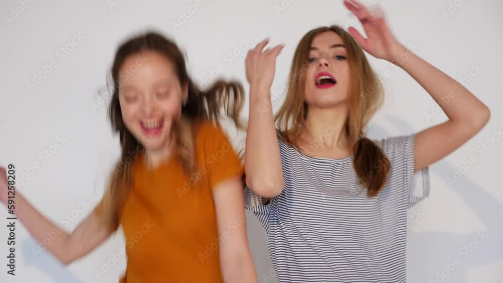Two carefree young girls going crazy. Women dancing in hipster Summer clothes. Positive smiling models isolated on white. Slow motion Two carefree young girls going crazy. Women dancing in hipster Summer clothes. Positive smiling models isolated on white. Slow motion