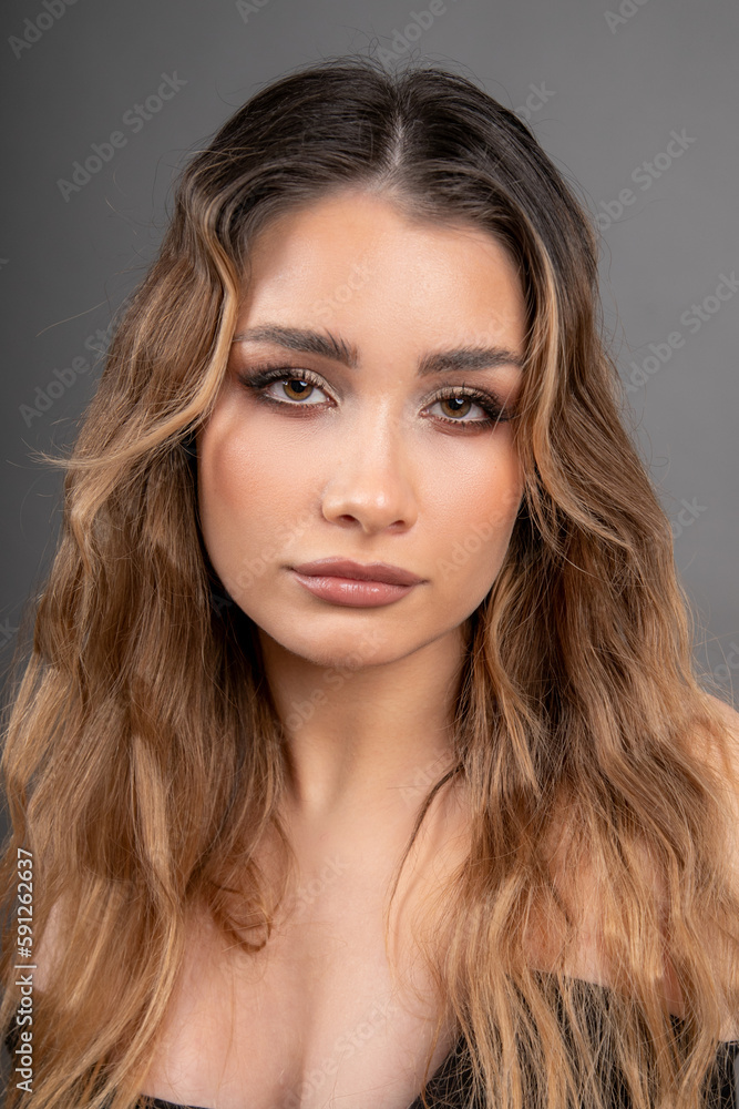 Fototapeta premium Portrait of face of young beautiful model with long well-groomed hair and professional makeup. Skin and hair care. 