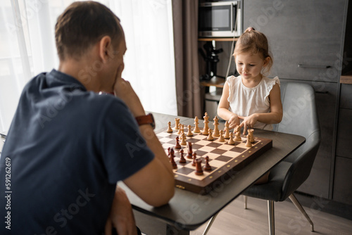 Father teaching his little daughter to play chess at the table in home kitchen. The concept early childhood development and education. Family leisure, communication and recreation.