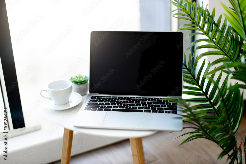 Wireless laptop placed on coffee table near white ceramic cup at bright office. Cozy and modern workplace of employee. Concept of technology for work. Wireless laptop placed on coffee table near white ceramic cup at bright office. Cozy and modern workplace of employee. Concept of technology for work.