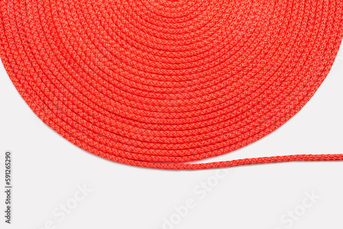 Red rope neatly twisted in a circle on a white background. Texture of red nylon rope close up. Roll of red rope. Free space for text. Neatly twisted textile rope