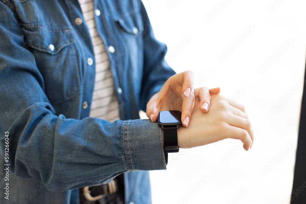 Crop of female office worker touching smartwatch on wrist while standing at workplace near window. Modern wireless gadget for work. Concept of electronic accessories.