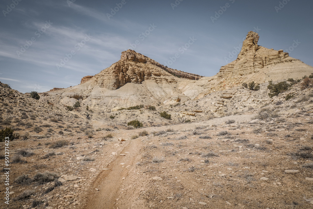 Curvy dirt trail through desert terrain in spring in central Utah near Goblin Valley underneath  rocky cliffs and mesas
