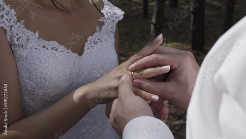 The bridegroom puts on a golden wedding ring to the bride in the forest