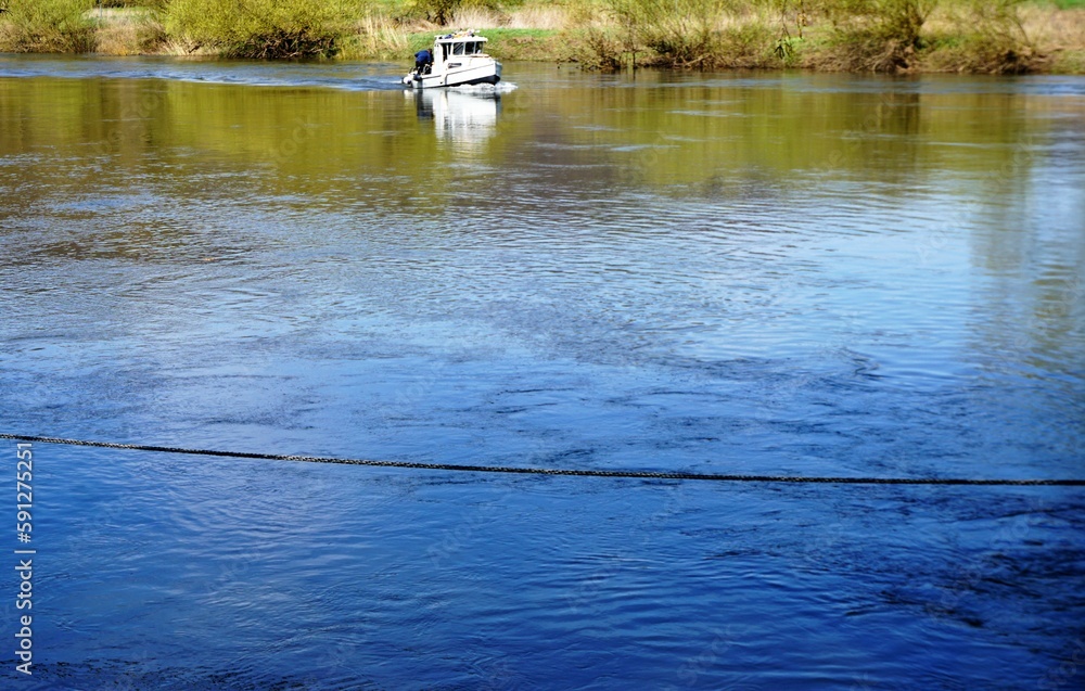 Flusslandschaft Panoram mit weißem Boot auf Wasser mit Spiegelung von Schilfgras vor Flusufer bei Sonne am Mittag im Frühling Flusslandschaft Panoram mit weißem Boot auf Wasser mit Spiegelung von Schilfgras vor Flusufer bei Sonne am Mittag im Frühling