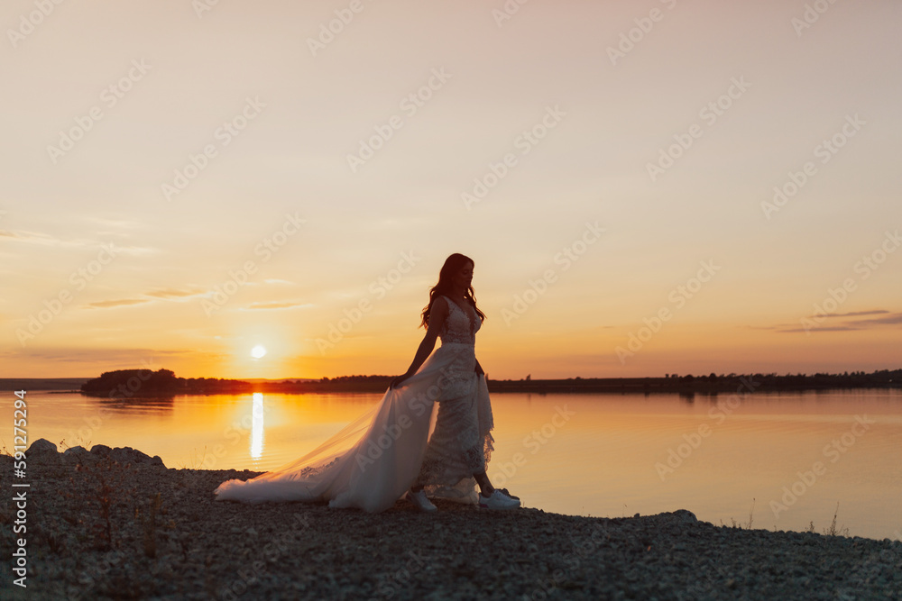 Beautiful bride in white long dress at amazing sunset on sea coast. Sun horizon. Wedding ceremony outdoors on the seashore. Copy space. Beautiful bride in white long dress at amazing sunset on sea coast. Sun horizon. Wedding ceremony outdoors on the seashore. Copy space.