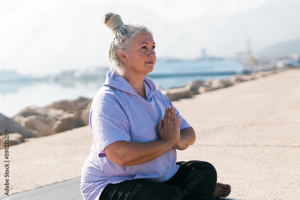 Mindful senior woman with dreadlocks meditating by the sea and beach - wellness and yoga practice