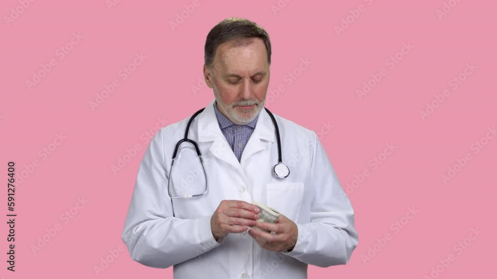 Smiling male doctor is counting money and puts it in his pocket. Isolated on pink. Smiling male doctor is counting money and puts it in his pocket. Isolated on pink.