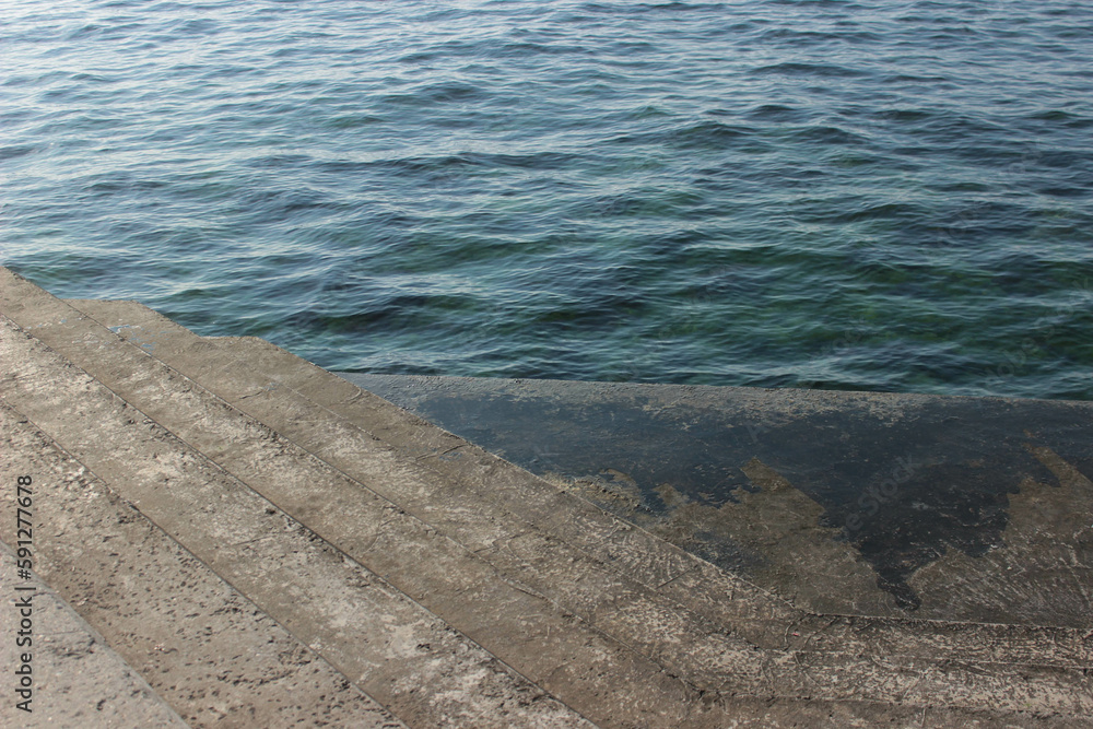 Obraz premium concrete embankment with stairs next to the blue sea in the sunshine on a spring and summer day