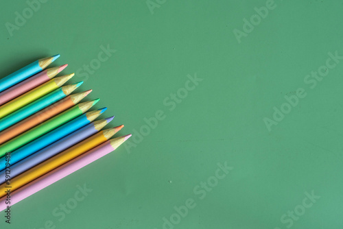 Pastel colored pencils, top view on green background, illustration concept, education and back to school