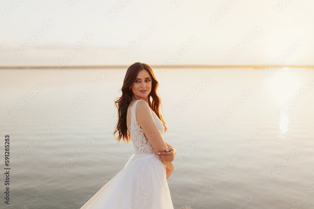 Beautiful smiling young bride is posing at the sea view Wedding ceremony outdoors on the seashore. Summer sunset. Beautiful smiling young bride is posing at the sea view Wedding ceremony outdoors on the seashore. Summer sunset.