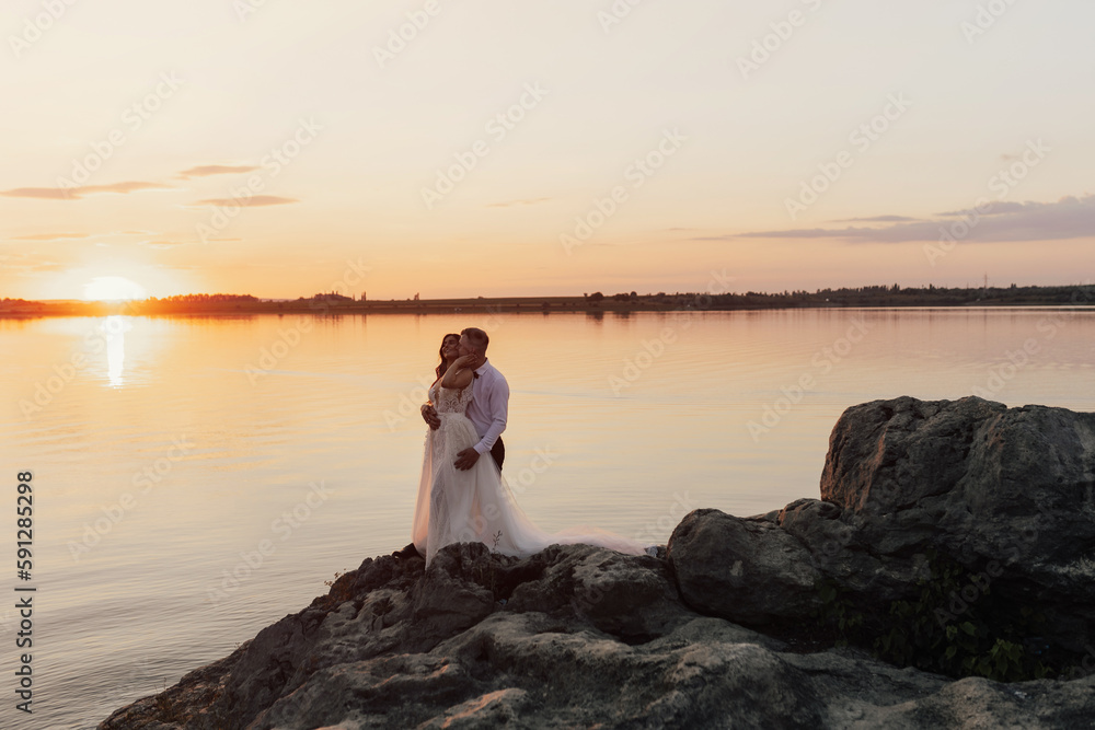 Newlyweds hugging on the rocky shore of the sea overlooking the sunset. Outdoor wedding ceremony on the sea. Newlyweds hugging on the rocky shore of the sea overlooking the sunset. Outdoor wedding ceremony on the sea.
