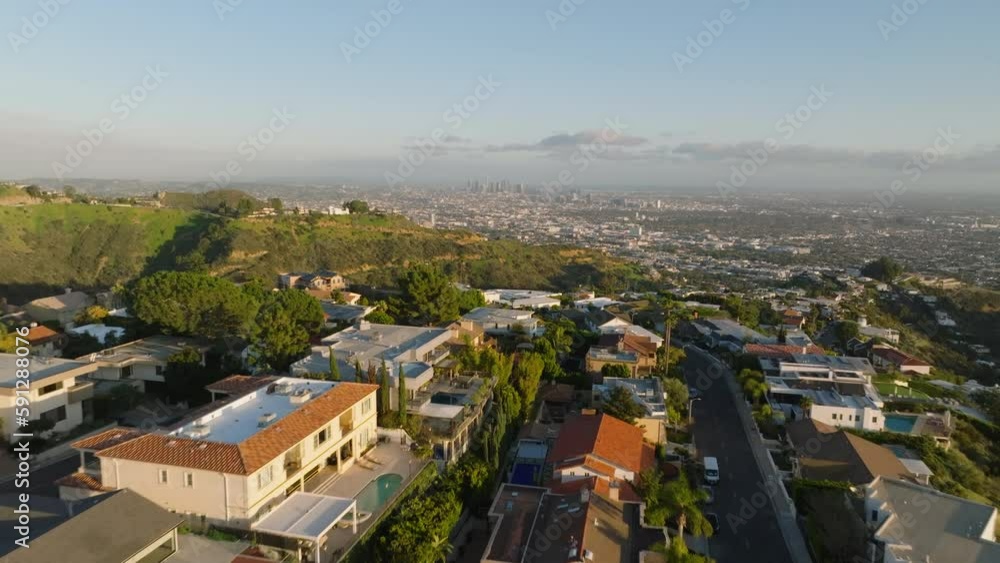 Forwards fly above deluxe homes in urban area situated on hills above metropolis lit by golden hour sunrays. Los Angeles, California, USA Forwards fly above deluxe homes in urban area situated on hills above metropolis lit by golden hour sunrays. Los Angeles, California, USA