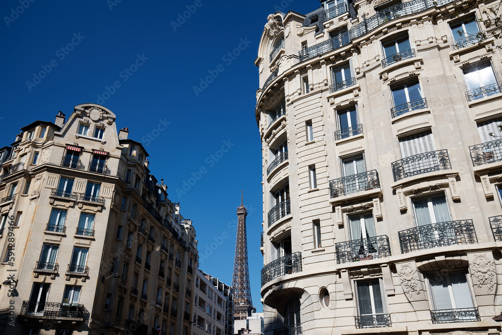 Traditional French houses with typical balconies and windows and Eiffel tower in the background . Paris.