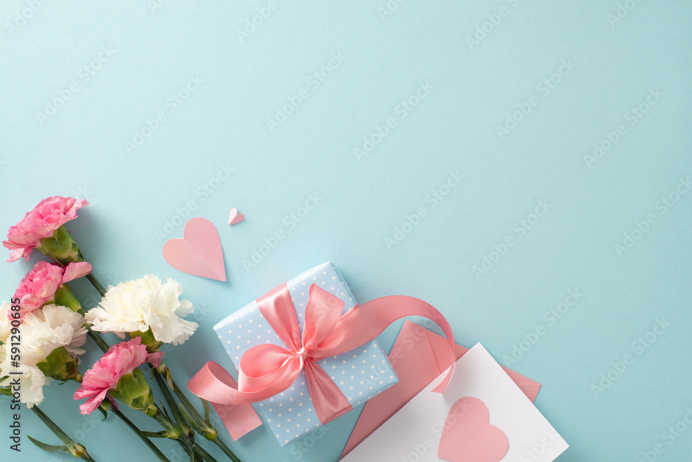 Mother's Day celebration concept. Top view flat lay photo of gift boxes with pink ribbons, carnation flowers, and pink paper hearts on pastel blue background with empty space for text or advert Mother's Day celebration concept. Top view flat lay photo of gift boxes with pink ribbons, carnation flowers, and pink paper hearts on pastel blue background with empty space for text or advert