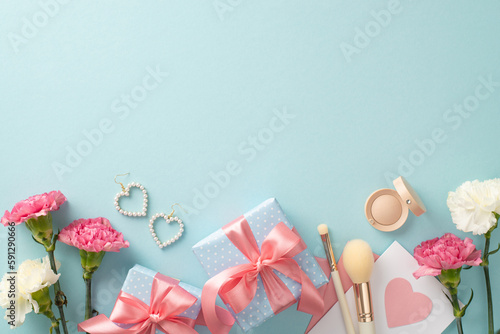 Mother's day concept. Top view flat lay photo of beautiful present boxes with pink ribbon, carnation flowers earrings makeup brushes on pastel blue background with empty space for text or advert