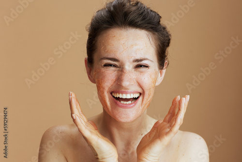 Fotografía smiling modern woman with face scrub against beige background