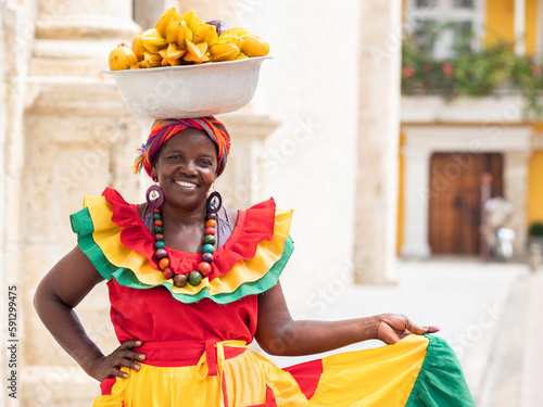 Smiling fresh fruit street vendor aka Palenquera in the Old Town of Cartagena de Indias, Colombia. Happy Afro-Colombian woman in traditional clothing, Colombian culture and lifestyle.	