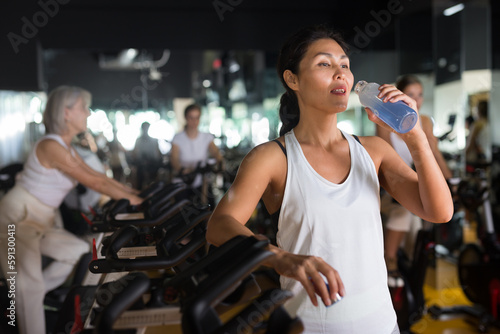 Portrait of asian woman who drinking water during cycling class in modern gym
