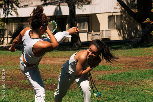 Принти на полотні mujeres practicando patadas, ejercicios y capoeira en la ciudad con su ropa de capoeira en un parque verde en un día soleado