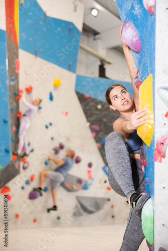 Young female alpinist practicing indoor rock-climbing on artificial boulder without the safety belts
