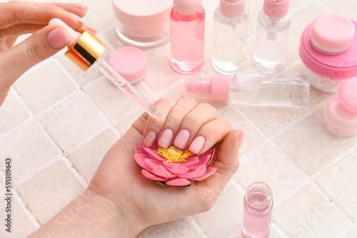 Female hands with bottle of cuticle oil  flower and different cosmetic products on light tile background  closeup