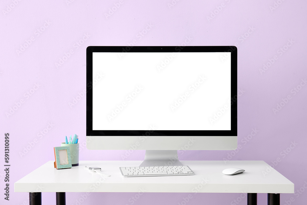 Workplace with computer, pen cup and smartwatch near lilac wall Workplace with computer, pen cup and smartwatch near lilac wall