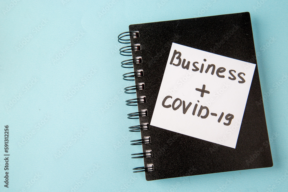 top view black copybook with business covid written sticker on blue