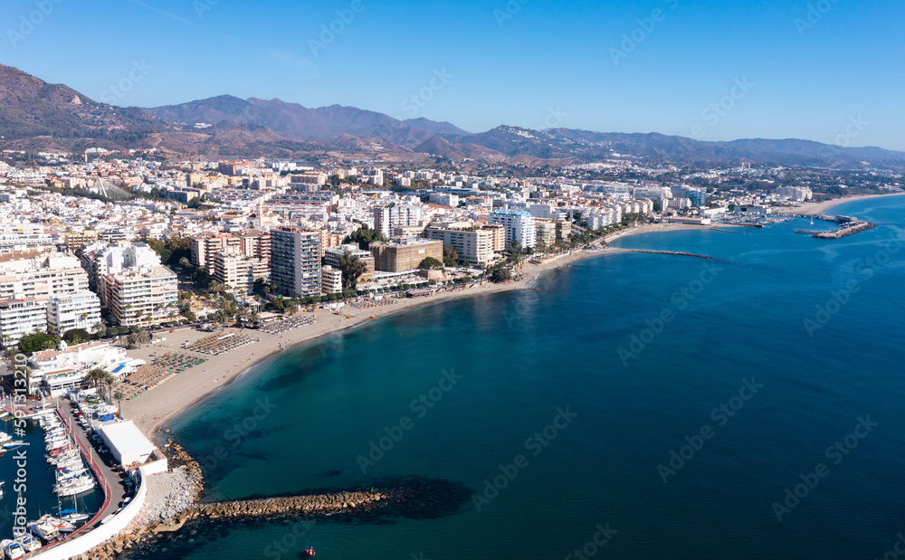 Aerial view of resort town of Marbella by Mediterranean coast in foothills of Sierra Blanca mountain range on sunny fall day, Spain