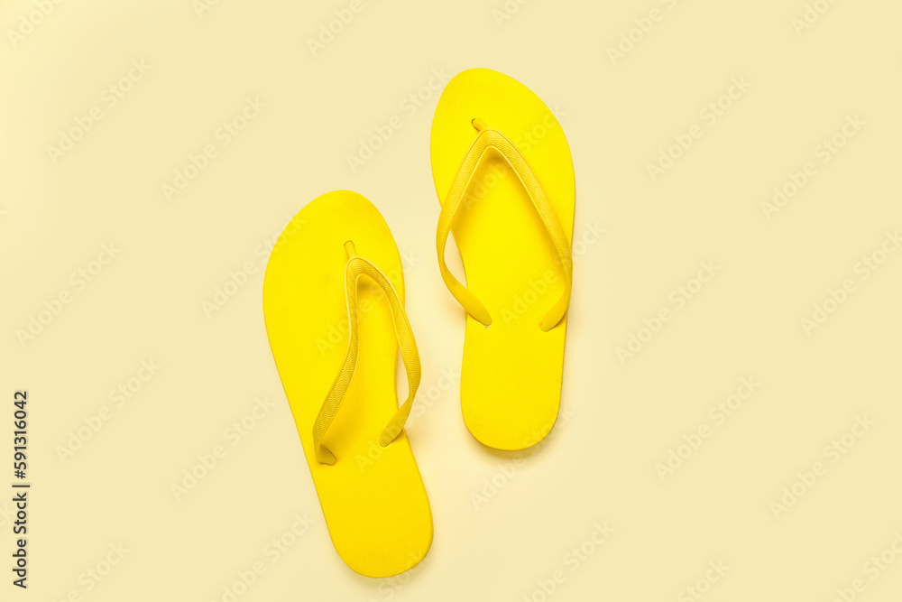 Fototapeta premium Yellow flip-flops on beige background, top view