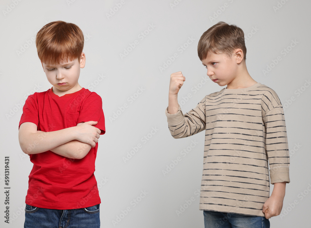 Boy with clenched fist looking at scared kid on light grey background. Children's bullying