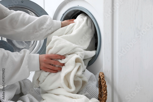 Woman putting dirty clothes in washing machine at home, closeup