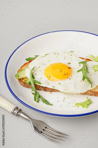 Delicious sandwich with fried egg, avocado and arugula on grey background