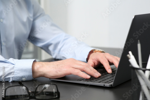 Man working on laptop at black desk in office, closeup