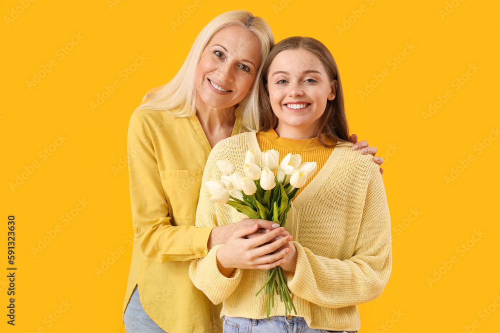 Young woman greeting her mother with tulips on orange background