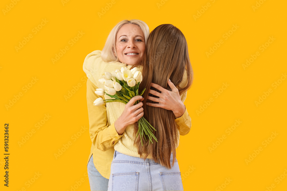 Mature woman with tulips hugging her daughter on orange background. Mother's Day celebration Mature woman with tulips hugging her daughter on orange background. Mother's Day celebration