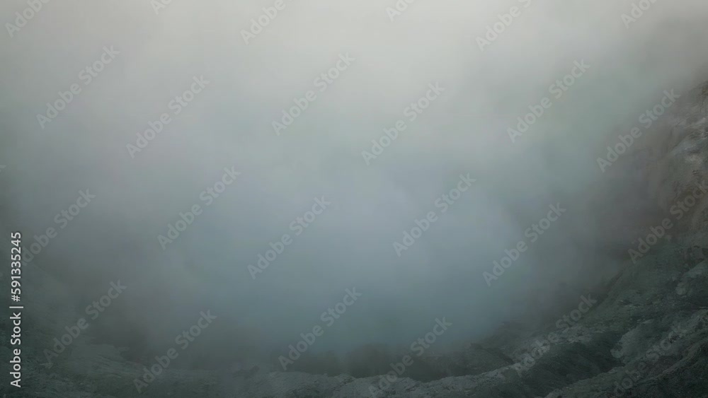 Top down drone view of smoke filled volcanic crater, panning up to reveal nearby volcanic mountains Top down drone view of smoke filled volcanic crater, panning up to reveal nearby volcanic mountains