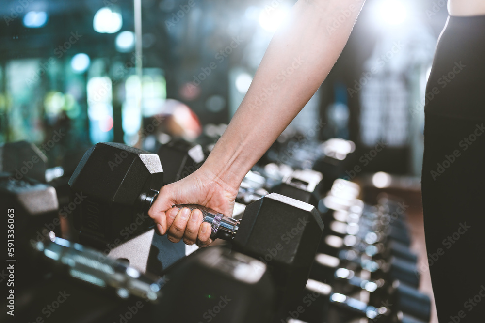 The strong hand of a woman holds the dumbbell for exercise body and muscle-building training gym with equipment, the lifestyle of a strong woman in indoor fitness with active motivation.